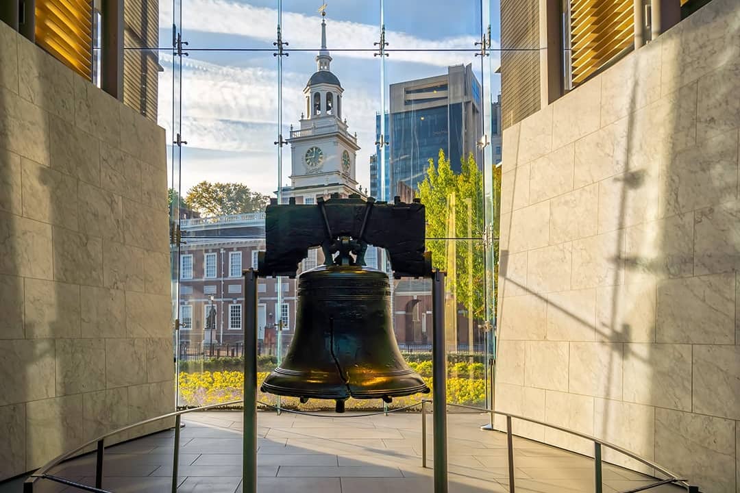 The Liberty Bell displayed inside the glass pavilion of the Liberty Bell Center, with the Independence Hall at the back in Philadelphia, Pennsylvania, USA.
